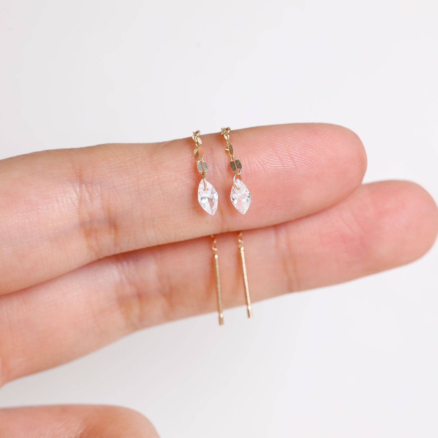 A pair of gold hoop earrings with marquise-cut clear crystals and small gold beads, held between fingers to show scale against a plain white background.