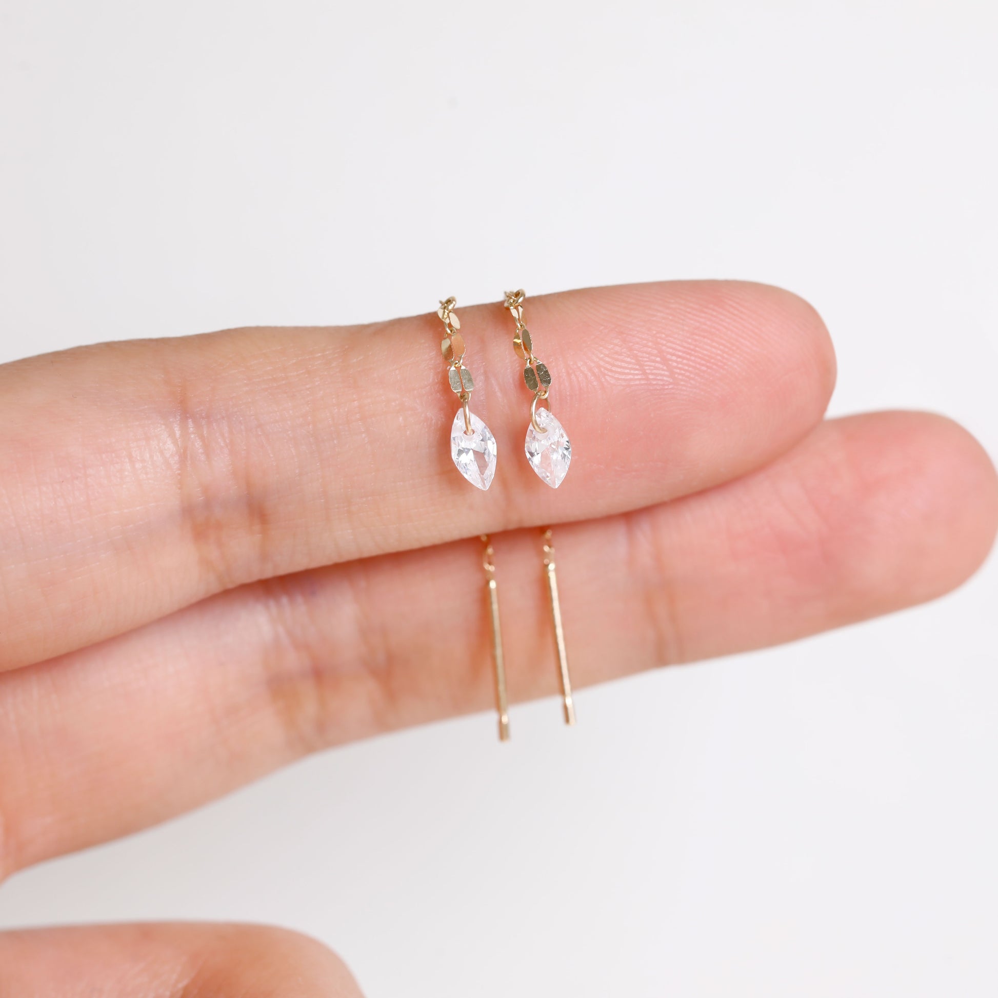 A pair of gold hoop earrings with marquise-cut clear crystals and small gold beads, held between fingers to show scale against a plain white background.