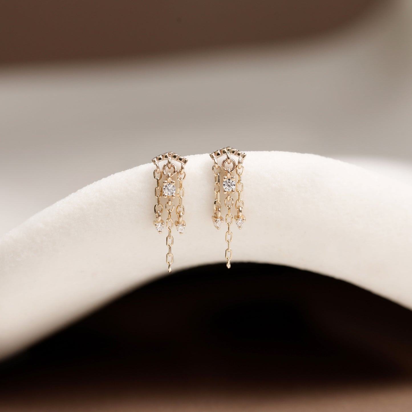 A pair of delicate gold dangle earrings with intricate filigree detailing and small clear stones, displayed on a white curved jewelry stand.