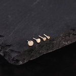 Choice of 14K gold stud earrings display on a dark stone surface