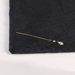 A delicate gold-toned ear cuff with a flat bar and a small clear teardrop crystal charm, displayed on a textured black slate surface.