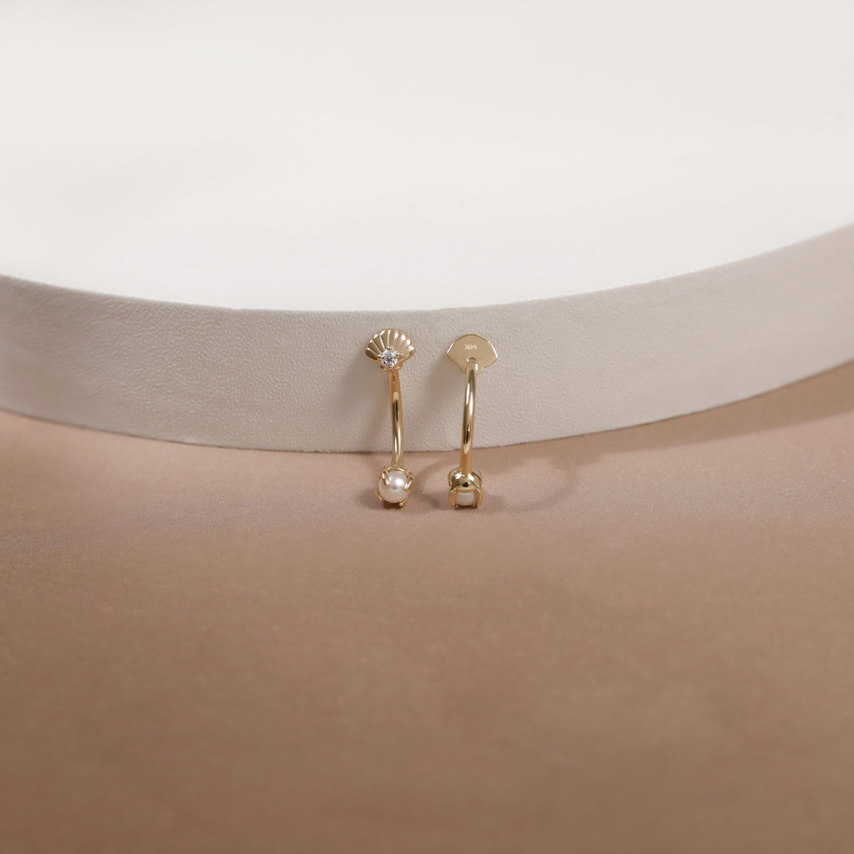A pair of small gold hoop earrings with clear faceted gemstones, displayed on a beige jewelry stand against a white background.