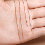 Three delicate gold and silver beaded chains with slim bar pendants resting on a person's palm.