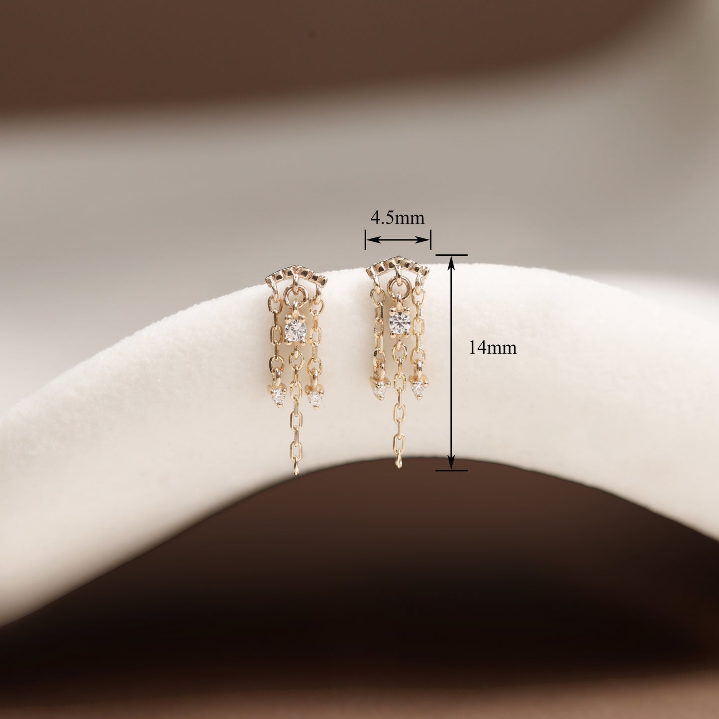 A pair of gold-toned dangling earrings displayed on a white curved jewelry stand, with measurement annotations showing 4.5mm width and 14mm height.