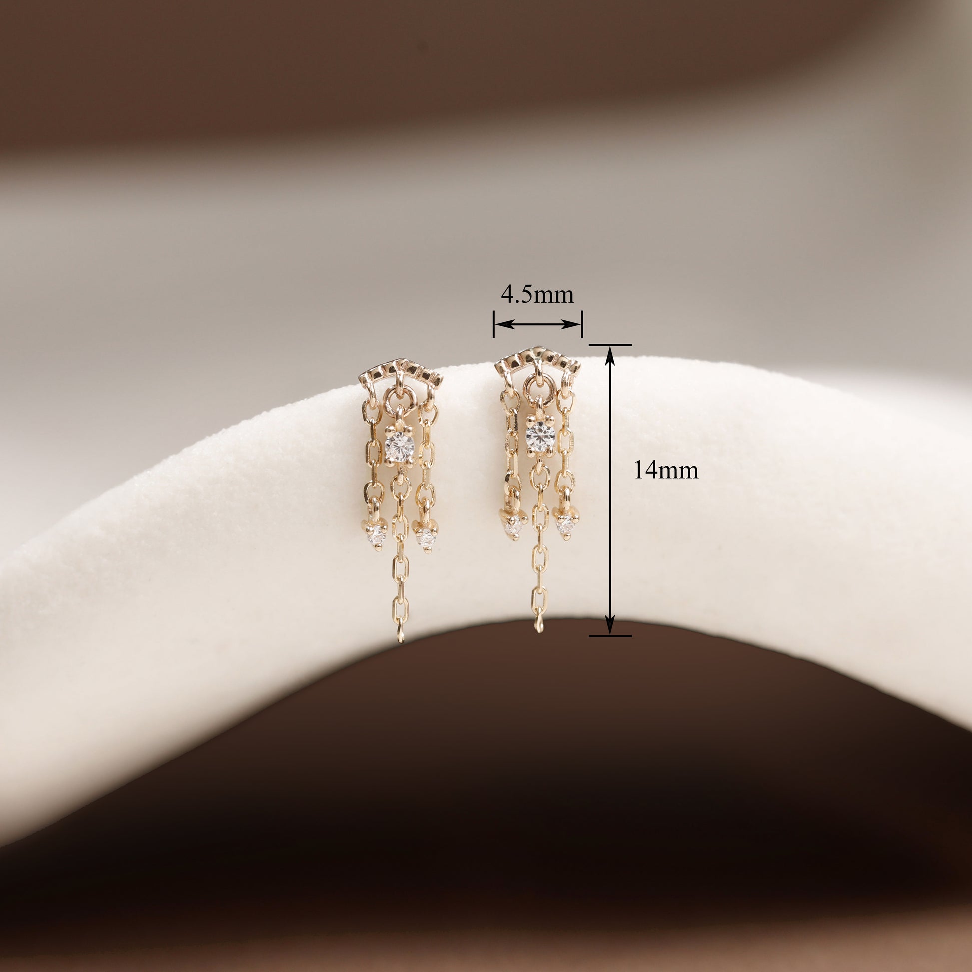 A pair of gold-toned dangling earrings displayed on a white curved jewelry stand, with measurement annotations showing 4.5mm width and 14mm height.