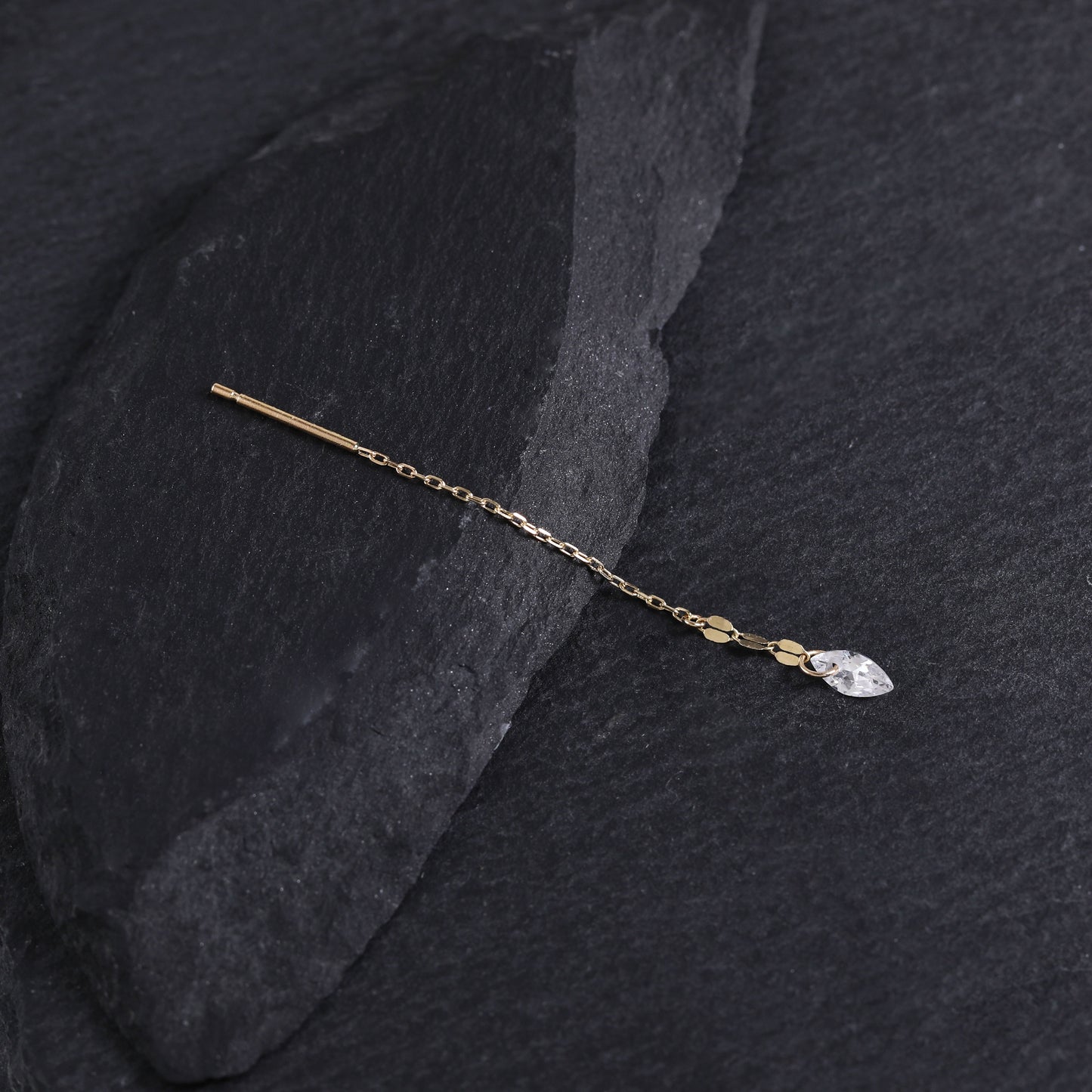 A delicate gold hair pin with a small clear marquise-cut crystal charm, displayed on a dark textured slate surface.
