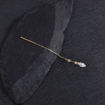 A delicate gold hair pin with a small clear marquise-cut crystal charm, displayed on a dark textured slate surface.