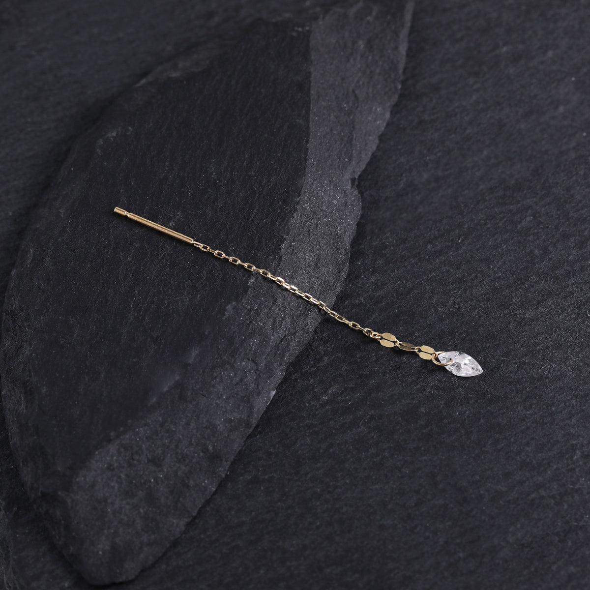 A delicate gold hair pin with a small clear marquise-cut crystal charm, displayed on a dark textured slate surface.