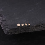 Set of gold stud earrings on a dark stone surface