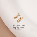 Two small gold charm pendants shaped like hands, each set with a clear gemstone, displayed on a white curved surface with black text listing dimensions.