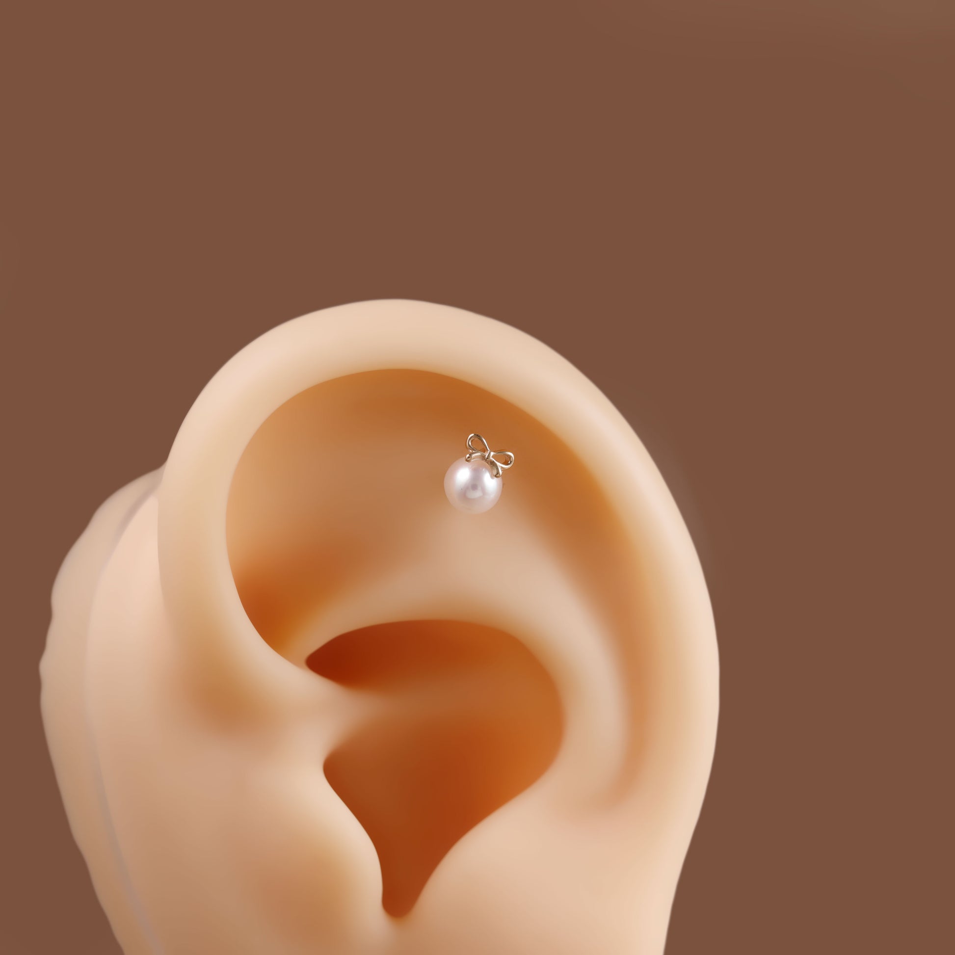 A small silver hoop earring with a single white pearl stud, shown worn on a beige ear model against a solid brown background.