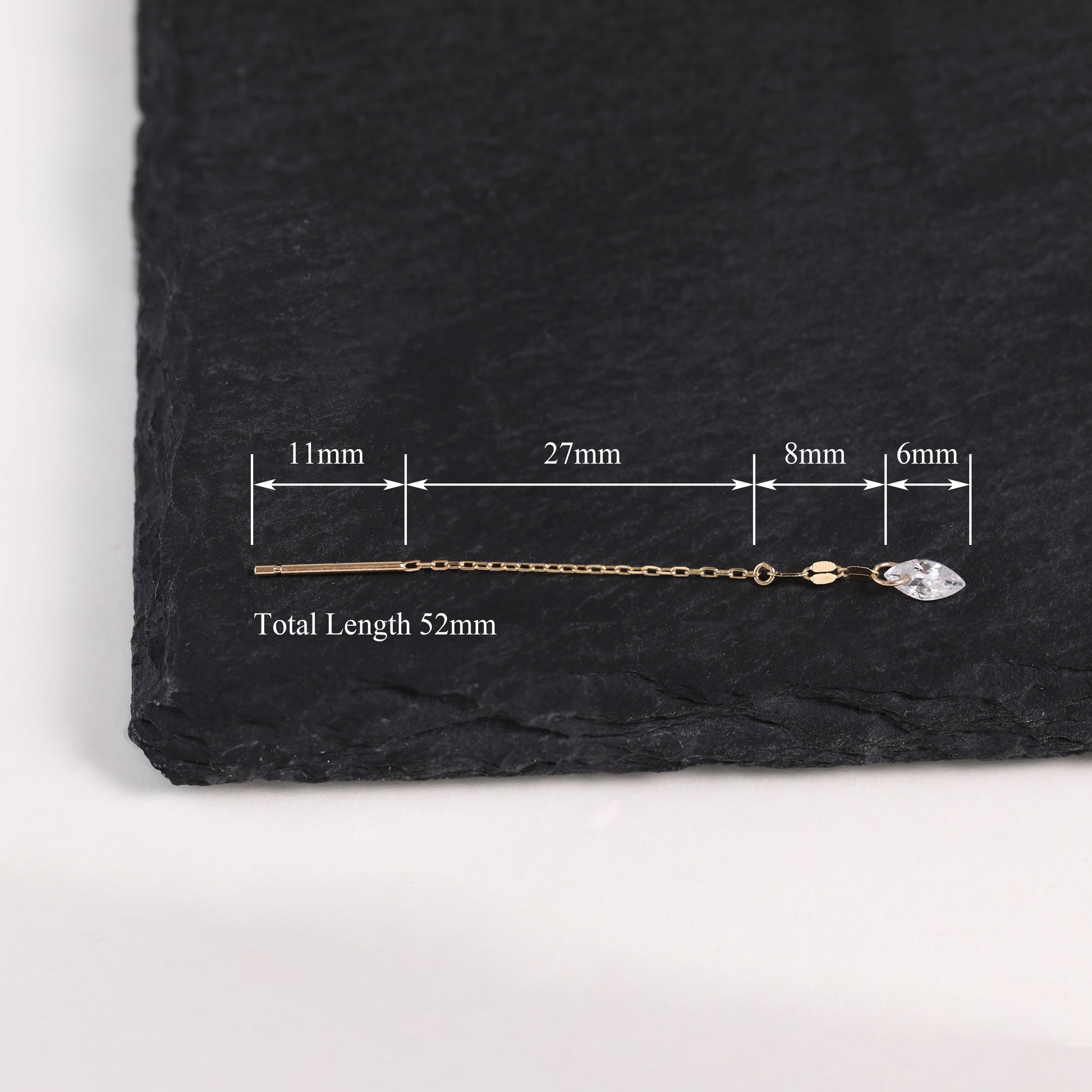 A gold-toned chain earring with a clear faceted stone, shown on a dark slate background with measurement annotations indicating a total length of 52mm.