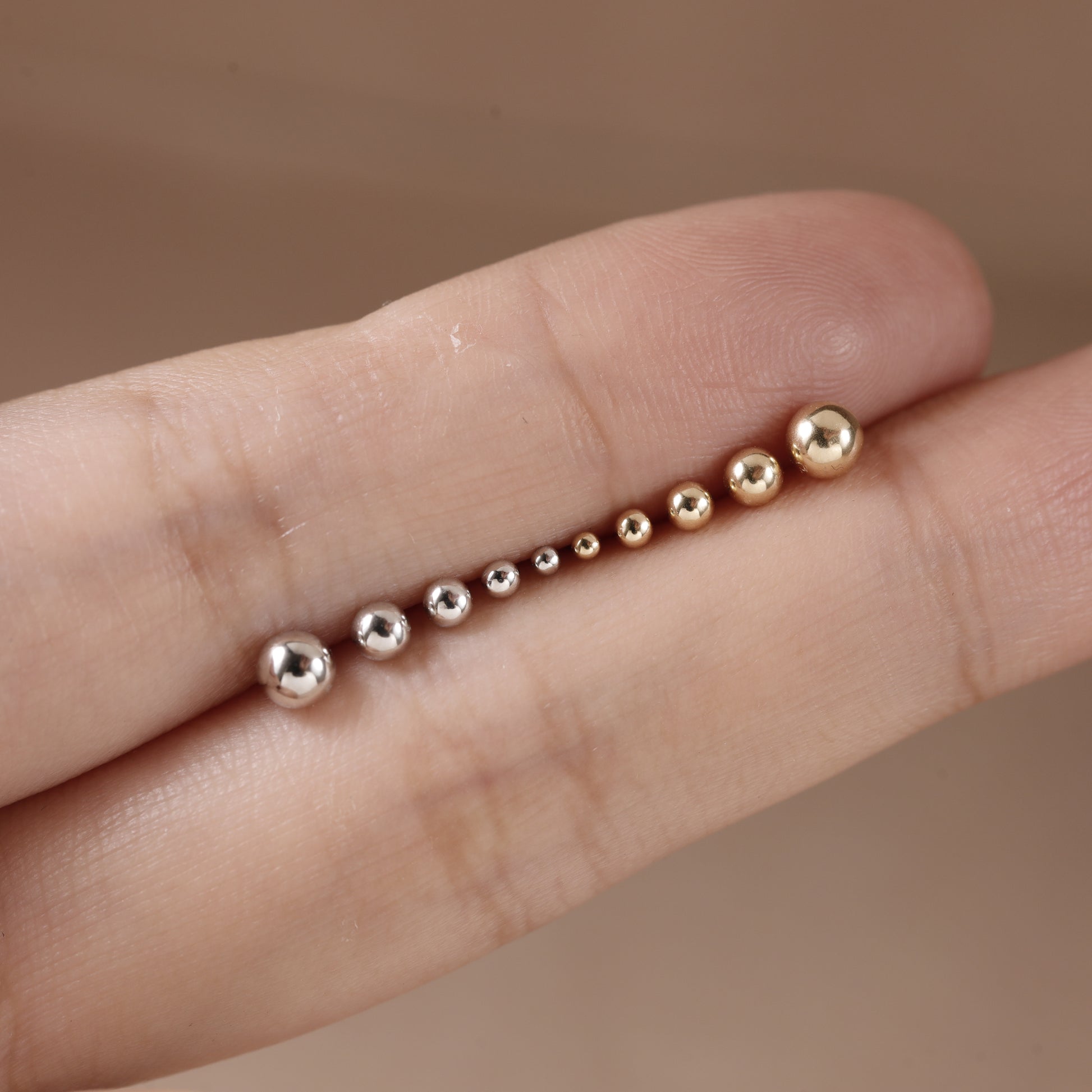 A close-up of a hand displaying a set of small metallic beaded rings in graduated sizes, showing rose gold and silver finishes.
