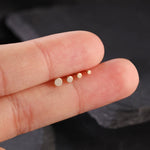 Small gold stud earrings held between fingers against a dark background