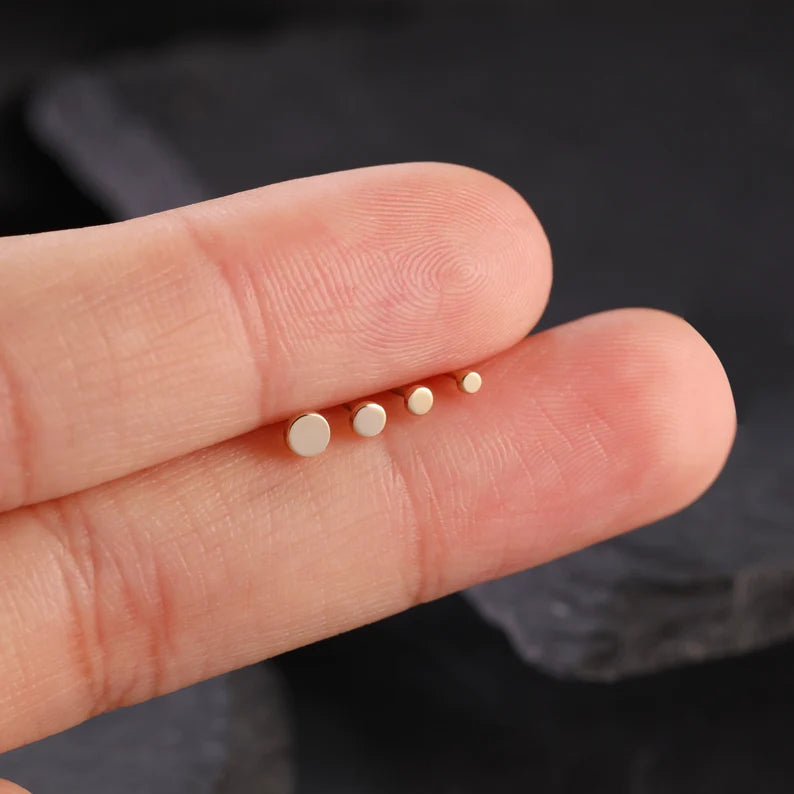Small gold stud earrings held between fingers against a dark background