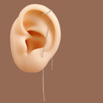A silver beaded chain ear cuff and matching drop earrings displayed on a beige anatomical ear model against a solid brown background.
