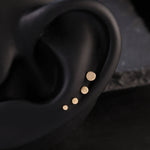Close-up of an ear with gold stud earrings on a dark background