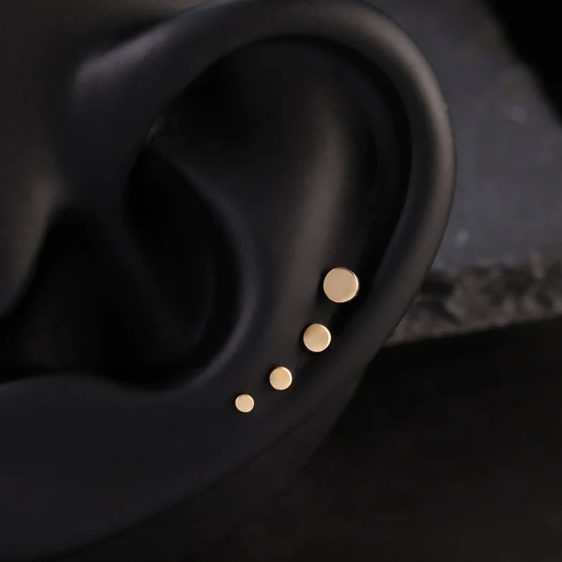 Close-up of an ear with gold stud earrings on a dark background