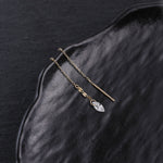 A pair of gold-toned drop earrings with a small clear faceted crystal pendant, displayed on a textured black surface.