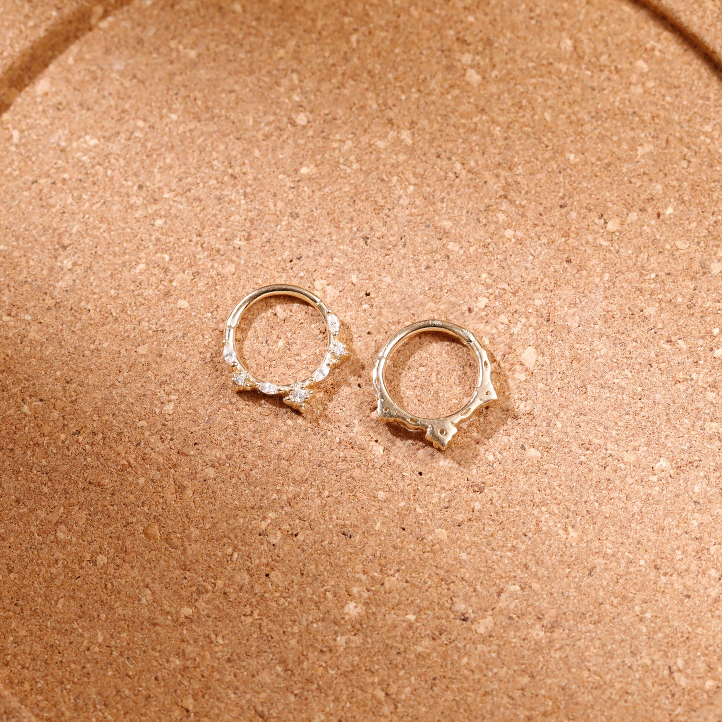 A pair of silver-toned hoop earrings with small clear stones set along the front, displayed on a textured brown surface.