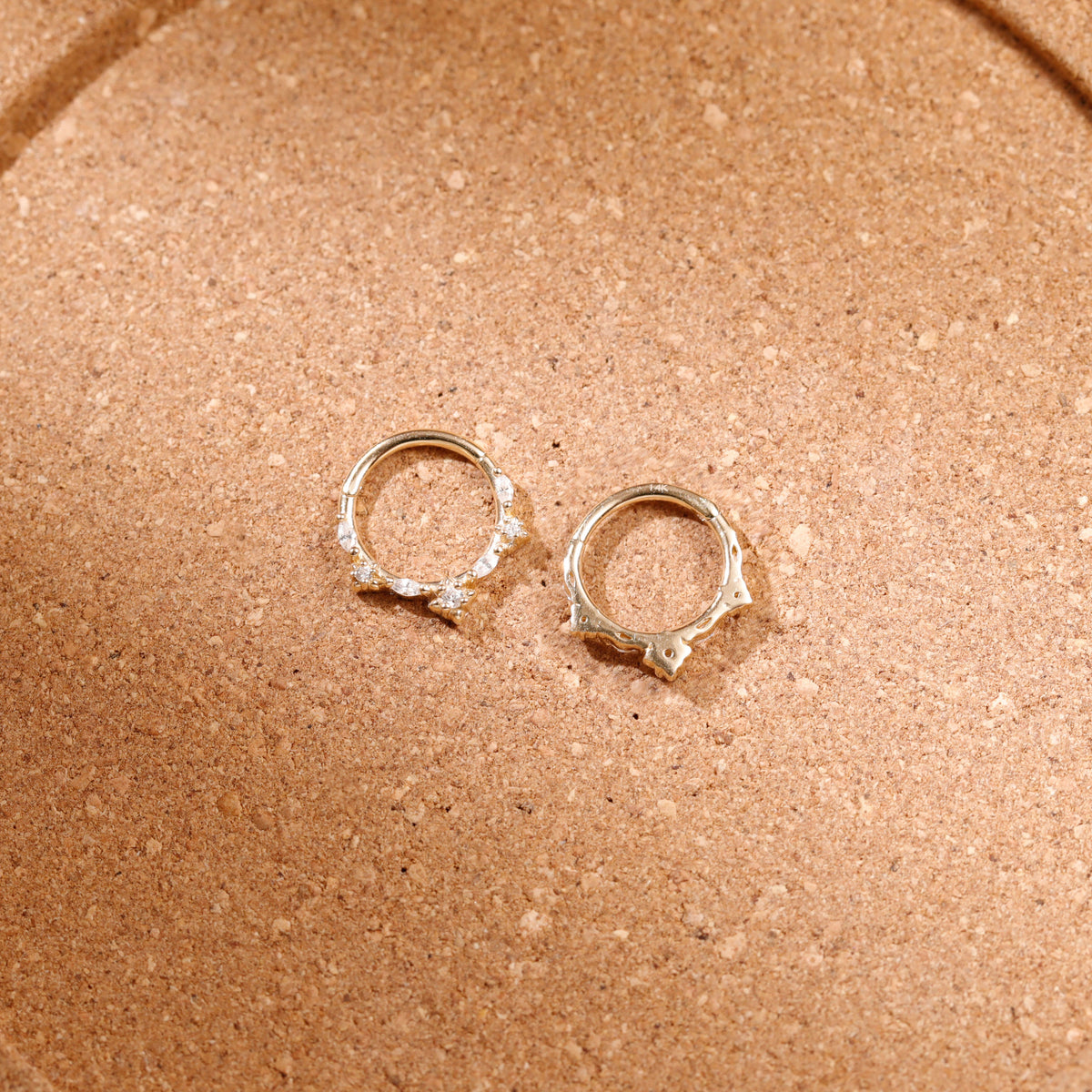 A pair of silver-toned hoop earrings with small clear stones set along the front, displayed on a textured brown surface.
