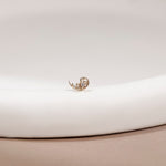A delicate gold crescent moon stud earring with intricate filigree detailing, resting on a white curved display stand.