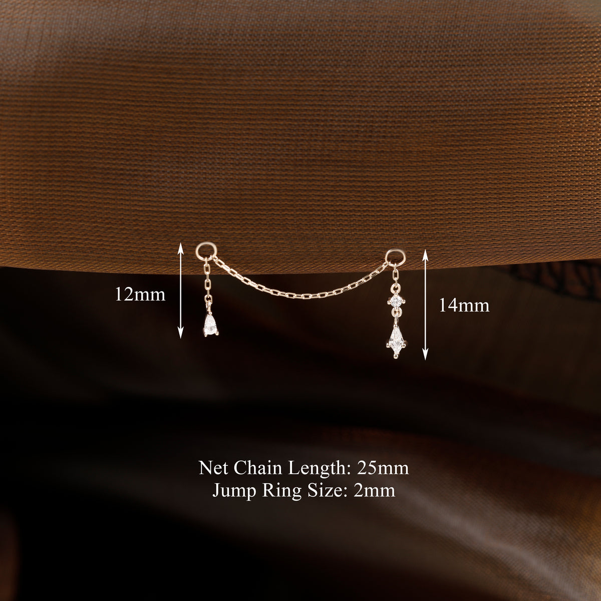A small gold-toned chain choker accessory with two dangling teardrop charms is shown against a brown textured fabric background, with measurement labels indicating 12mm and 14mm widths and text noting 25mm net chain length and 2mm jump ring size.