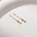 A pair of delicate gold dangle earrings with triangular charms, resting on a clean white surface.