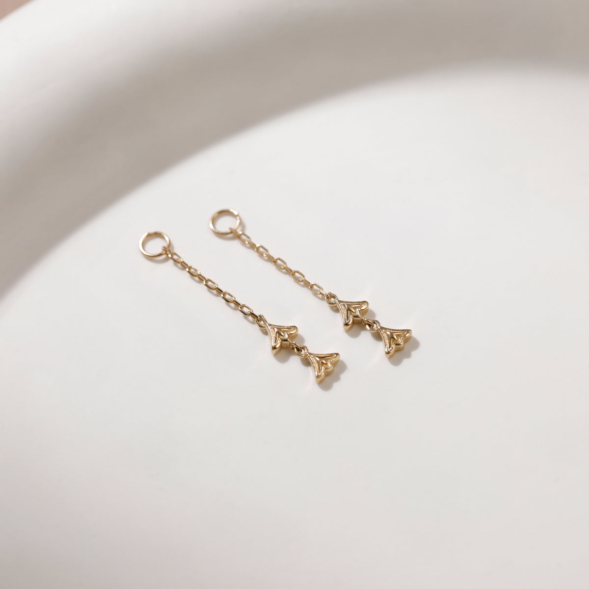 A pair of delicate gold dangle earrings with triangular charms, resting on a clean white surface.