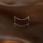 Two small gold chain link earrings with dangling loops, displayed on a textured dark brown fabric background.