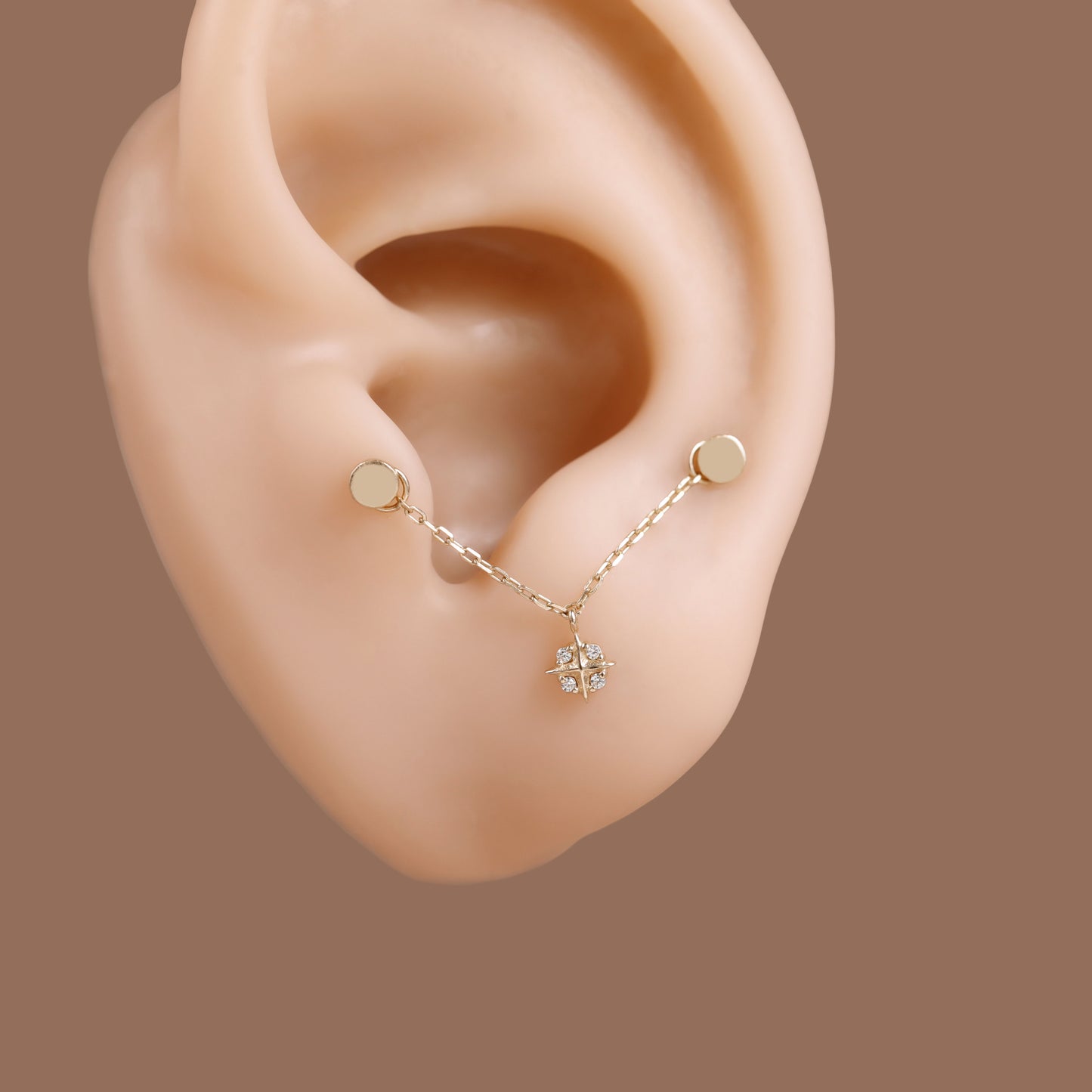 A gold lobe chain ear cuff with a small flower charm, displayed on a beige ear model against a solid brown background.