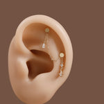 A pair of gold ear cuff earrings with dangling crystal charms, displayed on a beige silicone ear model against a solid brown background.