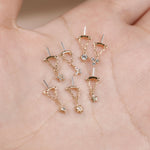 A set of nine delicate gold-toned dangle earrings displayed on an open palm. The earrings feature various celestial and geometric charms, including stars, moons, suns, and triangles, some adorned with clear rhinestones.