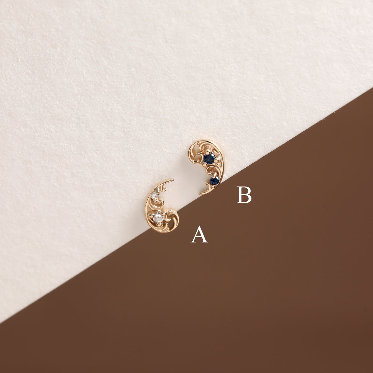 Two gold crescent moon stud earrings with blue and clear gemstones, labeled A and B on a split cream and brown background.