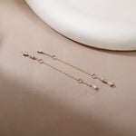 A pair of delicate rose gold chain earrings with small clear gemstone accents, displayed on a warm beige surface with a white ceramic plate in the background.