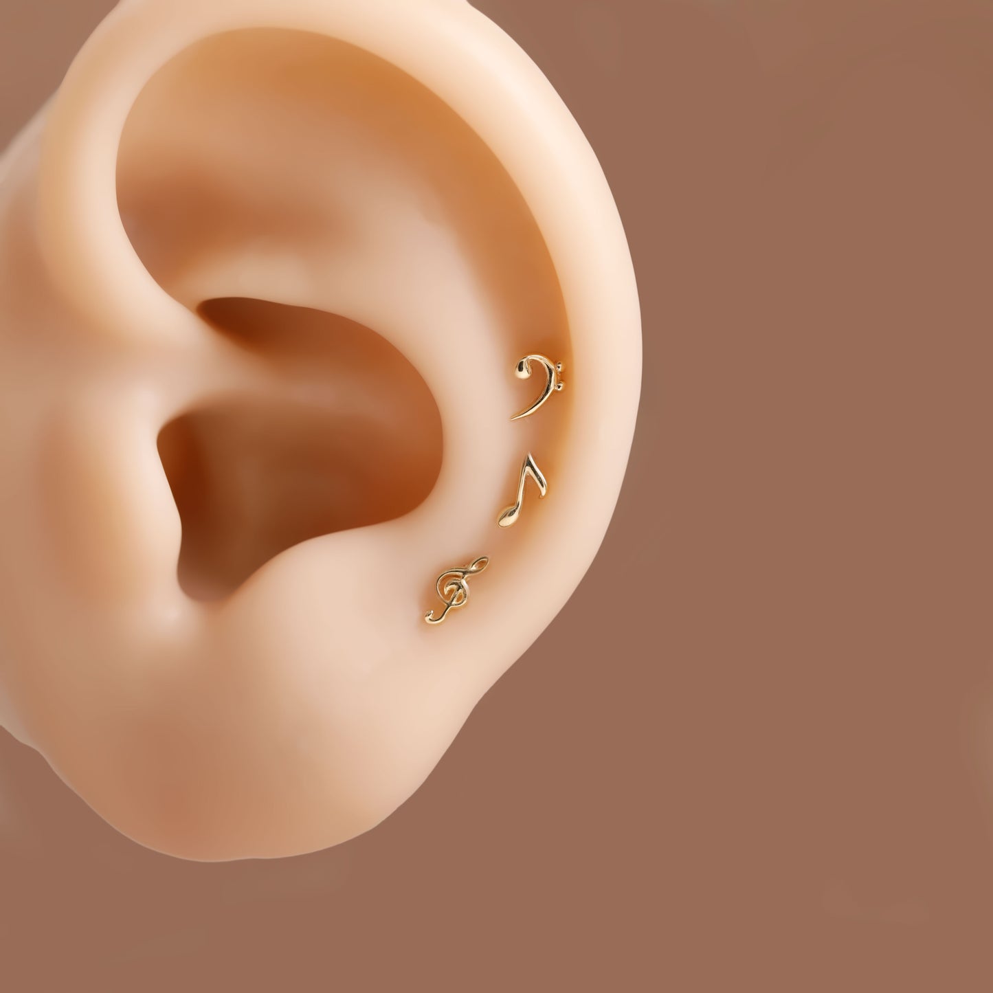 Three small gold ear cuff studs shown on a beige ear model against a warm brown background.