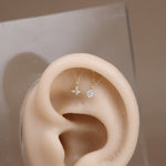A pair of delicate gold-tone ear cuff earrings with clear gemstones displayed on a beige silicone ear model against a neutral beige background.