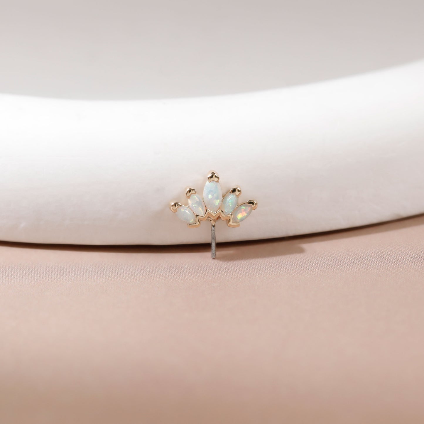 A small gold-toned stud earring with five iridescent white opal-like marquise-cut stones, displayed on a curved white jewelry stand against a soft beige background.