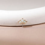 A small gold-toned stud earring with five iridescent white opal-like marquise-cut stones, displayed on a curved white jewelry stand against a soft beige background.