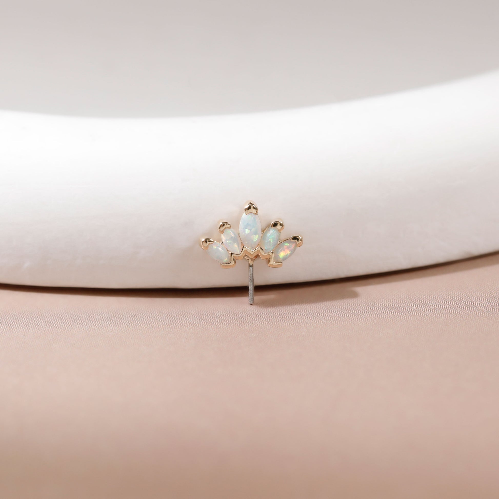 A small gold-toned stud earring with five iridescent white opal-like marquise-cut stones, displayed on a curved white jewelry stand against a soft beige background.