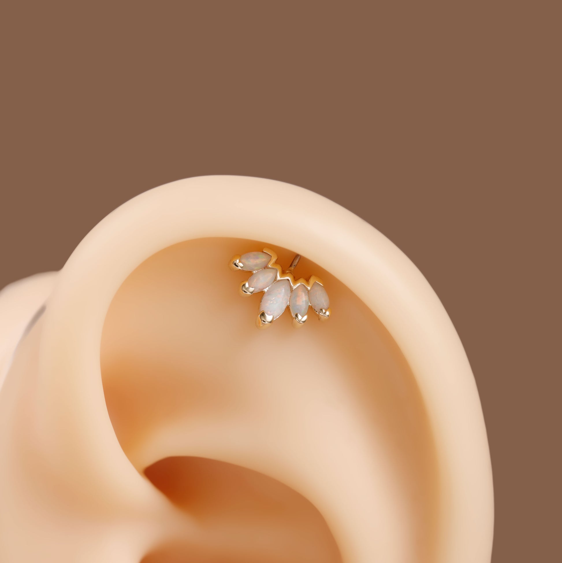 A close-up of a gold ear cuff with three small white teardrop-shaped crystals, shown worn on a beige ear display against a solid brown background.